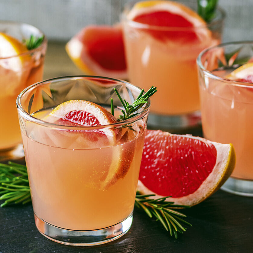 Fresh pink alcoholic cocktail with grapefruit, ice and rosemary, drink glass on a black stone board, old rustic style, selective focus, shallow depth of the field.